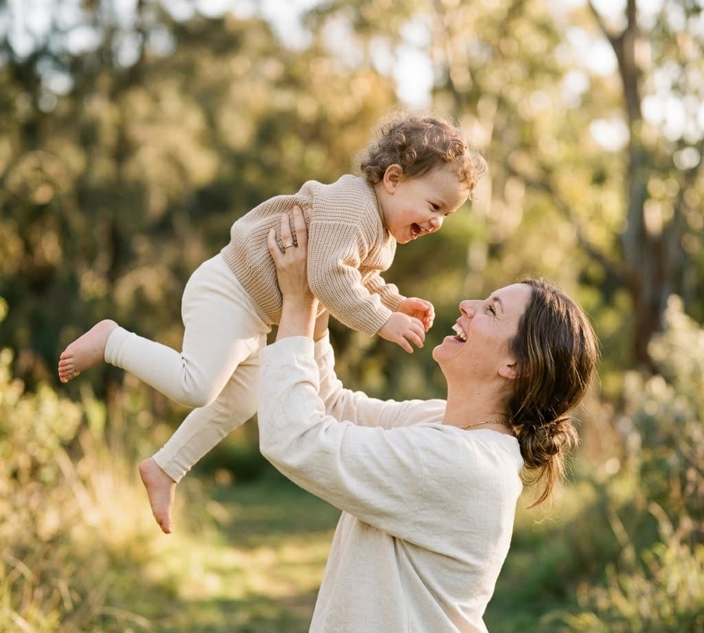 Elternteil hebt Kleinkind lachend in die Luft